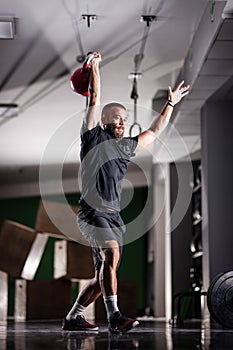 Muscular athlete power lifting a kettlebell. Man working out indoors