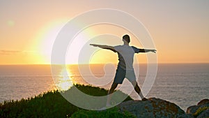 Muscular athlete silhouette stretching at sea rising sun. Strong man exercising