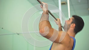 Muscular athlete in sportswear doing pull ups at gym. Young sportsman exercising on horizontal bar. Strong sporty man