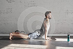 Muscular athlete tattooed body exercising workout in sunny sport club, brick wall. Fit shirtless male fitness model.