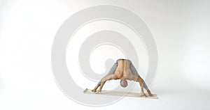 Muscular bald man with a bare torso and pants practices yoga poses on a yoga Mat on a white  background.