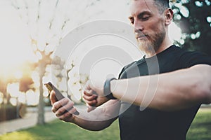 Muscular bearded athlete checking burned calories on smartphone application and smart watch after good workout session