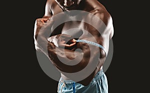 Muscular black bodybuilder measuring biceps with tape measure