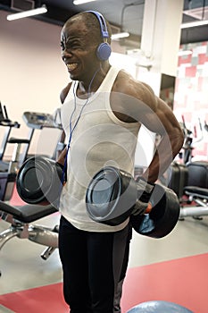 Muscular black man doing exercises with dumbbells at gym