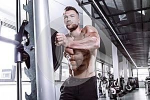 Muscular bodybuilder guy doing exercises with dumbbell on multipress