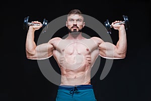 Muscular bodybuilder guy doing exercises with dumbbell over black background