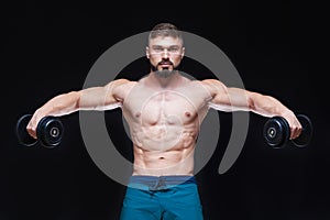 Muscular bodybuilder guy doing exercises with dumbbell over black background
