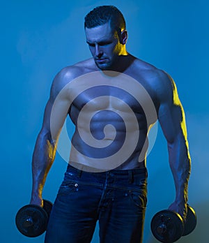 Muscular bodybuilder guy doing exercises with dumbbell over blue background.