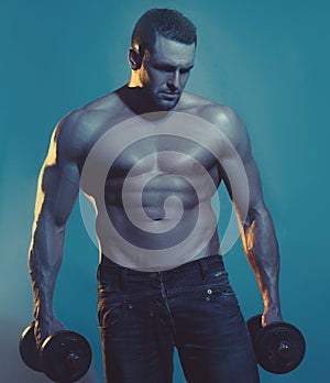 Muscular bodybuilder guy doing exercises with dumbbell over blue background.