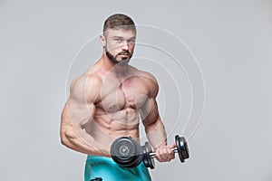 Muscular bodybuilder guy doing exercises with dumbbell over grey background