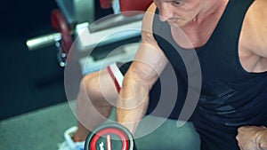 Muscular bodybuilder guy doing exercises with dumbbells in the gym.