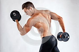 Muscular bodybuilder guy doing exercises with dumbbells over grey background with copyspace