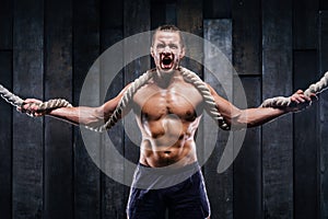 Muscular bodybuilder with heavy rope in hands and perfect body after training.