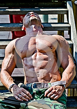 Muscular bodybuilder laying on wood stairs in the sun