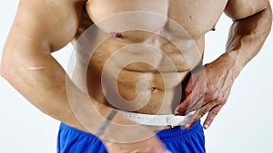 Muscular bodybuilder man measuring belly with tape measure