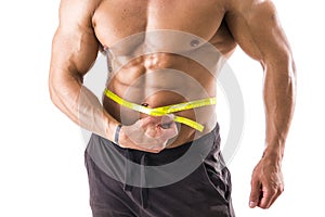 Muscular bodybuilder man measuring belly with tape measure