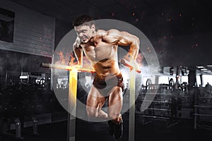 Muscular bodybuilder working out in gym doing exercises on burning fire parallel bars. Concept sport