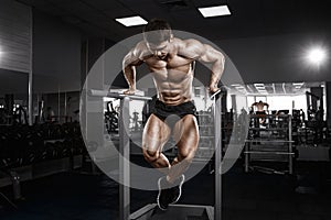 Muscular bodybuilder working out in gym doing exercises on parallel bars