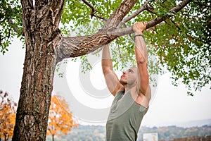 Muscular build man doing pull-ups in park