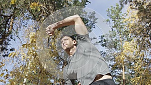 Muscular caucasian man in shirt stretching before workout doing standing side bends exercising in autumn forest at sunny