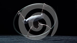Muscular circus artist perform Cyr Wheel on a black background. Concept of originality, creativity and outstanding