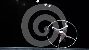 Muscular circus artist perform Cyr Wheel on a black background. Concept of willpower, motivation and healthy lifestyle