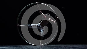Muscular circus artist perform Cyr Wheel on a black background. Concept of willpower, motivation and healthy lifestyle