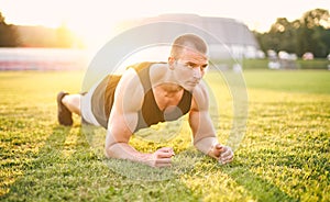 Muscular concentrated young man holding plank position outdoors in the grass in sunset - Morning warm up - Motivation and healthy