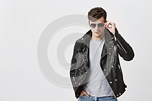 Muscular confident male posing indoors against gray background. Attractive handsome caucasian guy with trendy haircut in