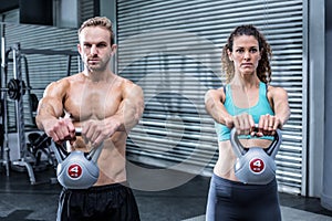 A muscular couple lifting kettlebells