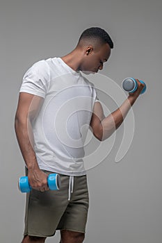 Muscular darkskinned man doing exercises with dumbbells