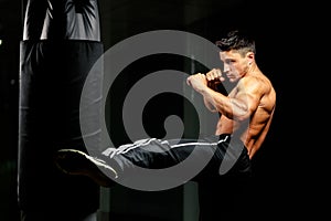 Muscular fighter leg middle kick to heavy bag