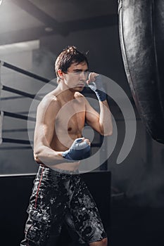 Muscular fighter prepare for practicing some kicks with punching bag