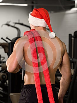 Muscular fit bodybuilder in santa claus cap with ropes on his shoulder