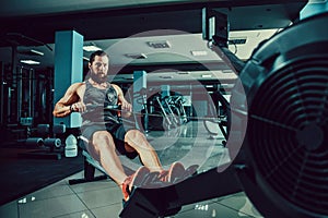 Muscular fit man using rowing machine at gym