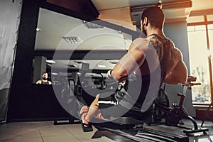 Muscular fit man using rowing machine at gym