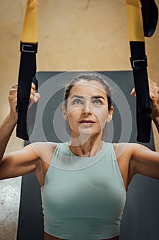 Muscular fit woman doing pull up exercise using suspension trainer.