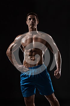 Muscular and fit young bodybuilder fitness male model posing over black background.