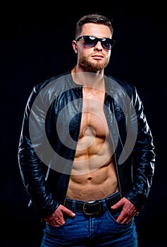 Muscular and fit young bodybuilder. Fitness male model posing over dark background. Leather jacket on naked torso.