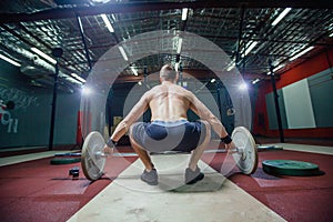 Muscular fitness man preparing to deadlift a barbell over his head in modern fitness center.Functional training.Snatch