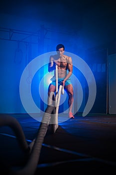 Muscular fitness man working out with battle ropes