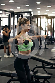 Muscular fitness woman athlete doing heavy weight exercise for shoulders with dumbbells in the gym