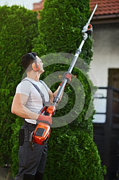 Muscular gardener trimming overgrown hedge outdoors