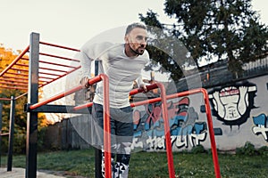 Muscular good looking man doing dips on parallel bars, chest workout outdoors