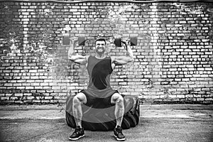 Muscular guy doing exercises with dumbbell against a brick wall