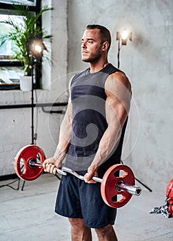 Muscular guy lifting barbell in studio room with spotlights