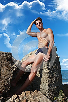 Muscular guy sitting on the rock, mediterranean Sea