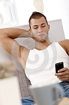 Muscular guy texting on sofa