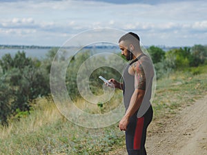 A muscular handsome bodybuilder with a tattoo on his shoulder listening music after a workout on a natural background.