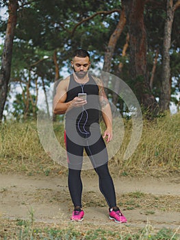 A muscular handsome bodybuilder with a tattoo on his shoulder listening music after a workout on a natural background.